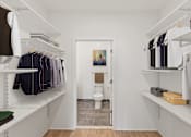 Thumbnail 26 of 66 - A white walk in closet with clothes hanging and a toilet in the background.