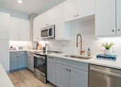 Thumbnail 15 of 47 - Modern kitchen with herringbone tile backsplash and blue cabinets at The Yancey Apartments, North Carolina