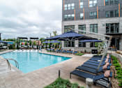 Thumbnail 18 of 47 - Swimming pool with lounge chairs and large umbrellas at The Yancey Apartments, Charlotte