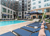 Thumbnail 16 of 47 - Poolside lounge area with navy blue chaise chairs at The Yancey Apartments, Charlotte, 28217