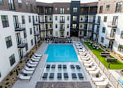 Thumbnail 2 of 30 - A large swimming pool surrounded by sun loungers and balconies of apartment buildings.