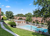 Thumbnail 20 of 23 - A pool surrounded by a fence and trees in front of a brick building.