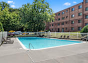 Thumbnail 21 of 23 - A swimming pool surrounded by a fence and trees in front of a brick building.