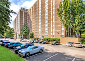 Thumbnail 2 of 16 - A parking lot with cars and a tall building in the background at Ashton Heights Apartments, Suitland, MD
