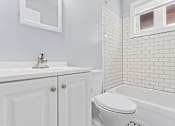 Thumbnail 5 of 14 - a bathroom with white subway tile and a white sink and toilet
