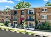 Thumbnail 5 of 6 - a brick apartment building with a red awning and trees in the background