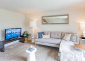 Thumbnail 2 of 10 - A living room with a grey couch, a white coffee table, and a television on a stand at Dutch Village Apartments, Maryland 21234