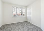 Thumbnail 24 of 29 - A room with a carpeted floor, a window with blinds, and a door.