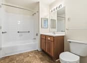 Thumbnail 27 of 29 - A white tiled bathroom with a wooden vanity and a white toilet.