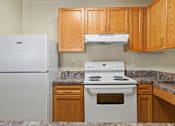 Thumbnail 16 of 29 - A kitchen with a white fridge, stove and wooden cabinets.