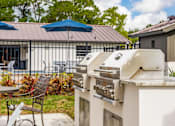 Thumbnail 5 of 17 - A grill is on a table outside with a blue umbrella and chairs.
