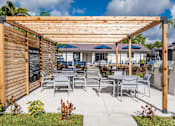 Thumbnail 7 of 17 - A wooden pergola with a sign and chairs under it.