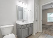 Thumbnail 10 of 20 - A bathroom with a white toilet, a sink with a mirror above it, and a cabinet.