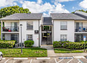 Thumbnail 9 of 17 - A white two-story apartment building with a black roof and a parking lot in front.