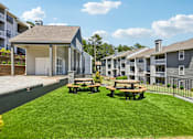 Thumbnail 7 of 40 - A sunny day at the apartment complex with picnic tables in the grassy courtyard.