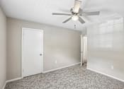 Thumbnail 18 of 37 - A room with a ceiling fan and carpeted floor.