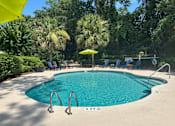 Thumbnail 2 of 16 - A swimming pool surrounded by trees and chairs.