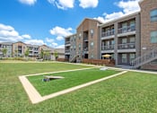 Thumbnail 43 of 44 - A grassy area in front of apartment buildings with a small toy airplane on the ground.