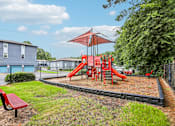 Thumbnail 27 of 37 - A playground with a red slide and a red bench.