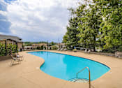 Thumbnail 16 of 27 - A large outdoor swimming pool surrounded by trees and a fence.