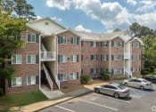 Thumbnail 7 of 18 - a brick apartment building with stairs and cars parked in a parking lot