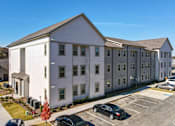 Thumbnail 21 of 27 - a large white apartment building with cars parked in front of it