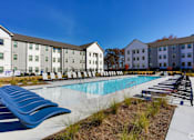 Thumbnail 17 of 27 - a swimming pool with chaise lounge chairs in front of an apartment building