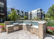 Thumbnail 3 of 32 - an outdoor kitchen with two grills next to a pool with an apartment building in the background at Century University City, Charlotte, NC