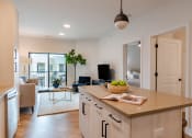 Thumbnail 20 of 28 - a kitchen island with a bowl of fruit on it and a living room in the background  at Century West Pryor, Lee's Summit, MO