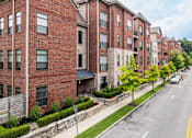 Thumbnail 58 of 62 - A row of red brick apartment buildings line a tree-lined street.