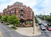 Thumbnail 59 of 62 - A street view of a red brick building with cars parked on the side of the road.