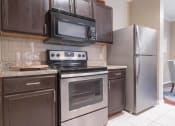 Thumbnail 21 of 29 - a kitchen with dark cabinets and stainless steel appliances at Century South Shore, League City