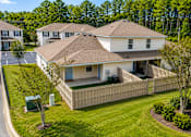 Thumbnail 19 of 21 - A house with a brown roof and a white exterior is surrounded by a wooden fence and green bushes.