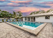 Thumbnail 16 of 17 - A swimming pool surrounded by a brick patio and a white building.