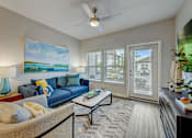 Thumbnail 3 of 39 - a living room with a blue couch and a ceiling fan at Century Mundy Mill Apartments, Oakwood 30566