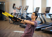 Thumbnail 23 of 39 - a young man exercising in a gym with a weights machine at Century Mundy Mill Apartments, Oakwood, Georgia