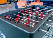 Thumbnail 22 of 36 - A foosball table with red and black players is in the foreground.