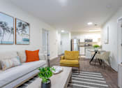 Thumbnail 2 of 31 - A living room with a white couch, a yellow chair, and a dining table with chairs.
