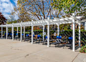 Thumbnail 11 of 31 - A white pergola with blue chairs is in the foreground of a sunny day.