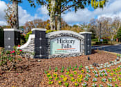 Thumbnail 1 of 31 - A sign for Hickory Falls Apartment Homes is surrounded by flowers and trees.