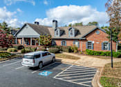 Thumbnail 17 of 31 - A silver minivan is parked in a handicapped spot in front of a brick building.