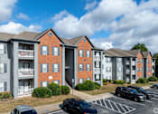 Thumbnail 24 of 31 - Apartment complex with a parking lot in front.