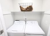 Thumbnail 8 of 21 - A laundry basket with a cat in it sits on top of a shelf above two washing machines.