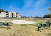 Thumbnail 9 of 31 - A park with two benches and a playground in front of apartment buildings.