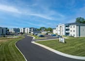 Thumbnail 30 of 31 - A road curves through a grassy area with apartment buildings in the background.
