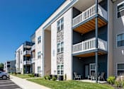 Thumbnail 15 of 31 - A modern apartment building with a parking lot in front.