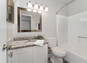 Thumbnail 6 of 23 - A white bathroom with a granite countertop and a white toilet.