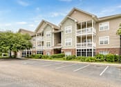 Thumbnail 22 of 31 - A large apartment complex with a parking lot in front.