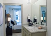 Thumbnail 9 of 36 - A bathroom with a sink, mirror, and a bedroom in the background.