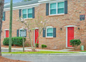 Thumbnail 2 of 29 - a brick building with red doors and green shuttered windows at Savan Pointe Townhomes East and West, Savannah Georgia